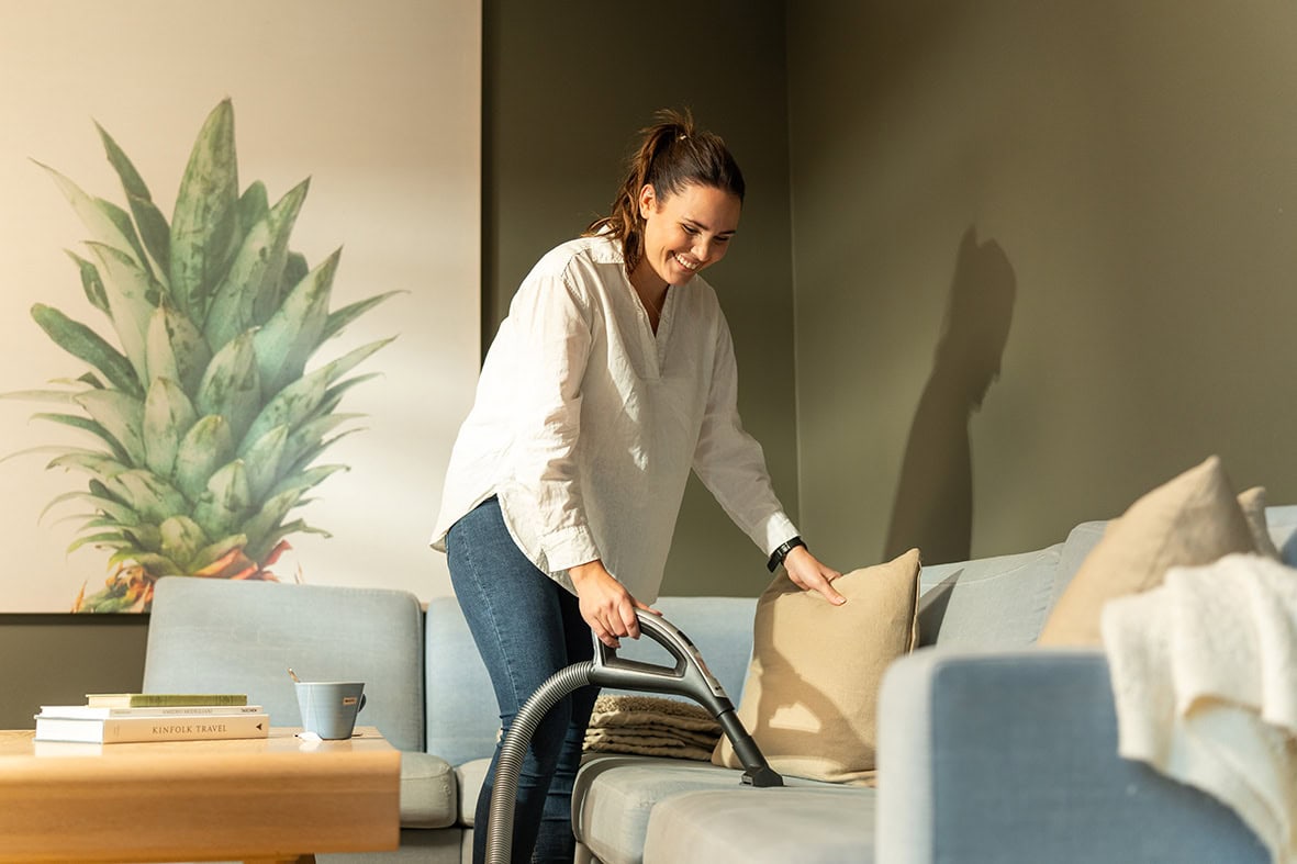 Kvinne som rengjør sofa i stue med moderne innemiljø og komfort.
