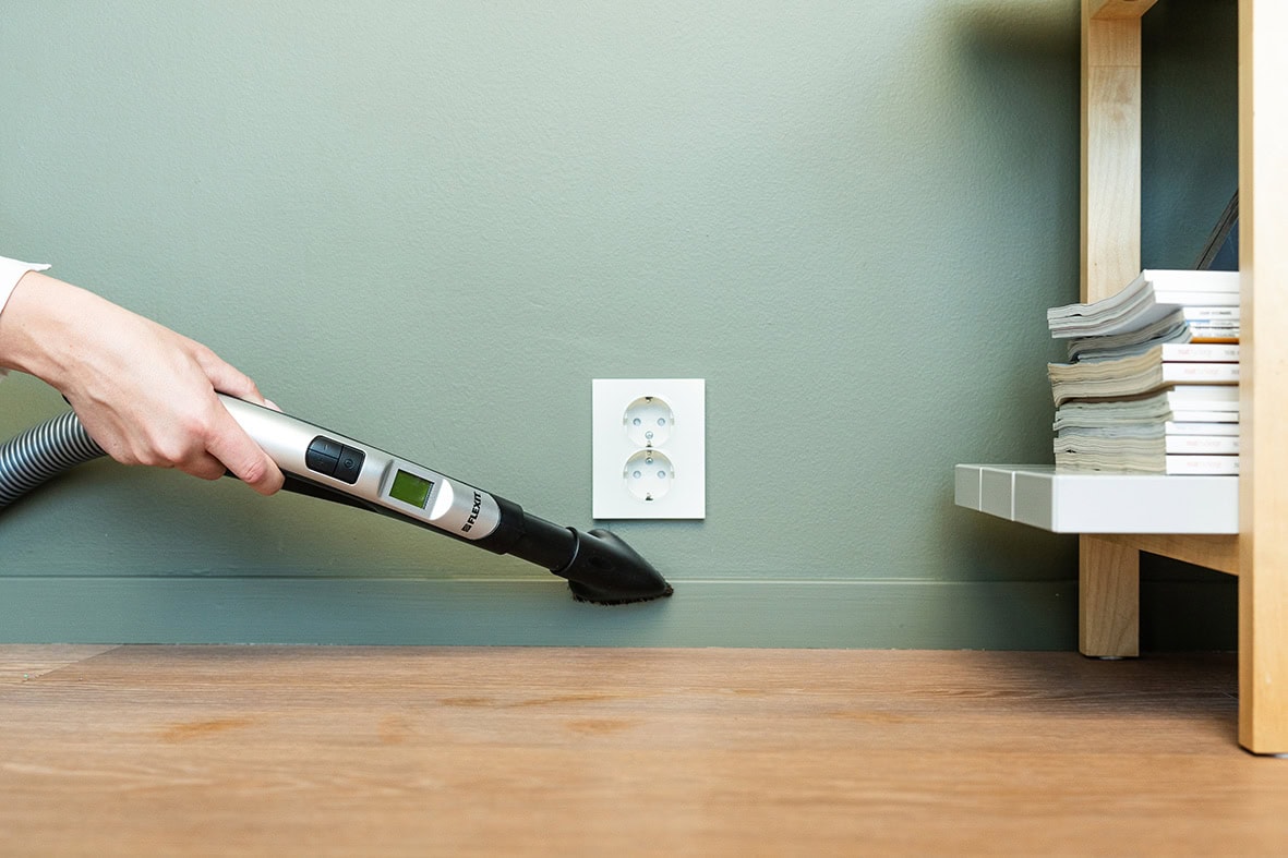 Effektiv støvrengjøring med støvsuger på gulv nær vegg og stikkontakt.