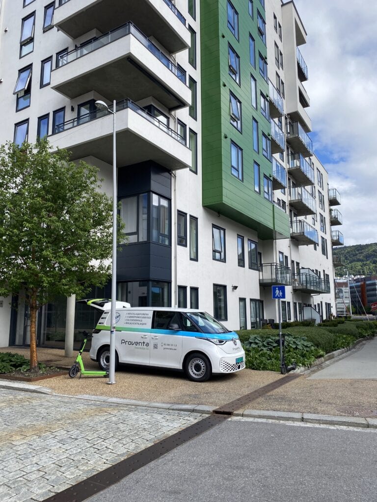 Bilde av moderne boligbygg med grønne og hvite fasadeelementer, parkering og bymiljø.